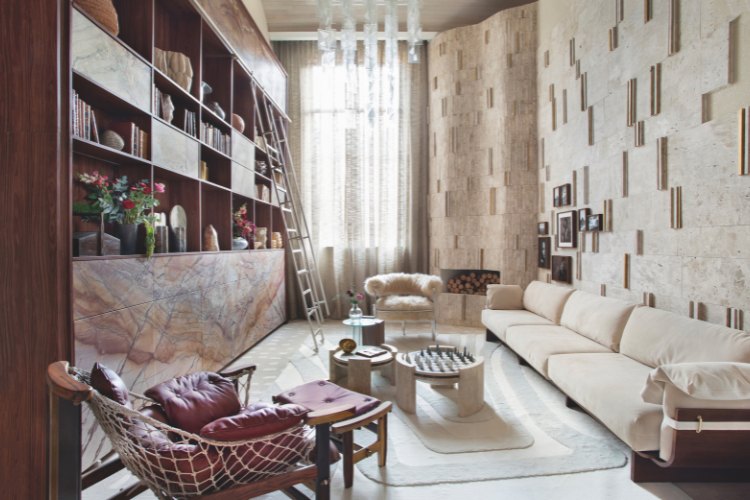 Casacor-Sao-Paulo-2025-9 Sala com estante, parede de texturas, poltrona bordô, piso travertino Bahia