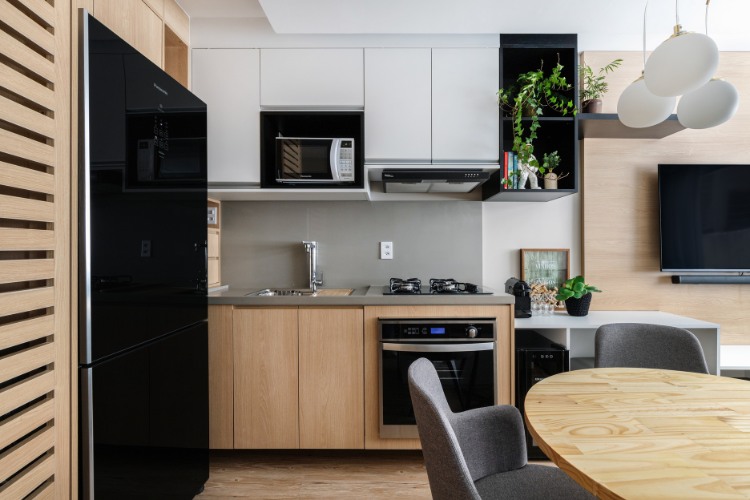 Estudio-De-29-M2-1 Cozinha em MDF branco e em madeira, com parede cinza, plantas e geladeira preta