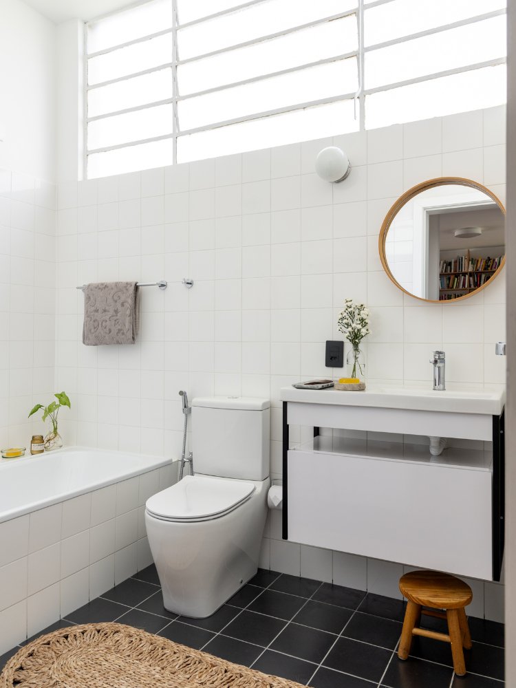 Reforma-Apartamento-100-M2-4 Visão mais geral do banheiro, com banheira, vaso sanitário, pia, gabinete e espelho redondo