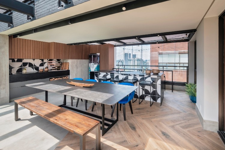 Apartamento-Duplex-De-350Mc2B2-11 Área externa com mesa grande com banco e cadeiras azuis, balcão com banquetas, cozinha com azulejos pretos e brancos