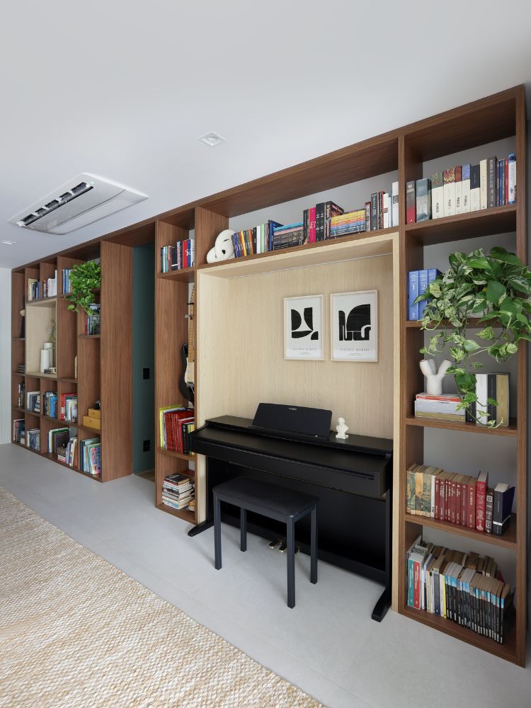 Apartamento-Decorado-158-M2-2 Estante de madeira com livros, espaço com piano e porta para área íntima