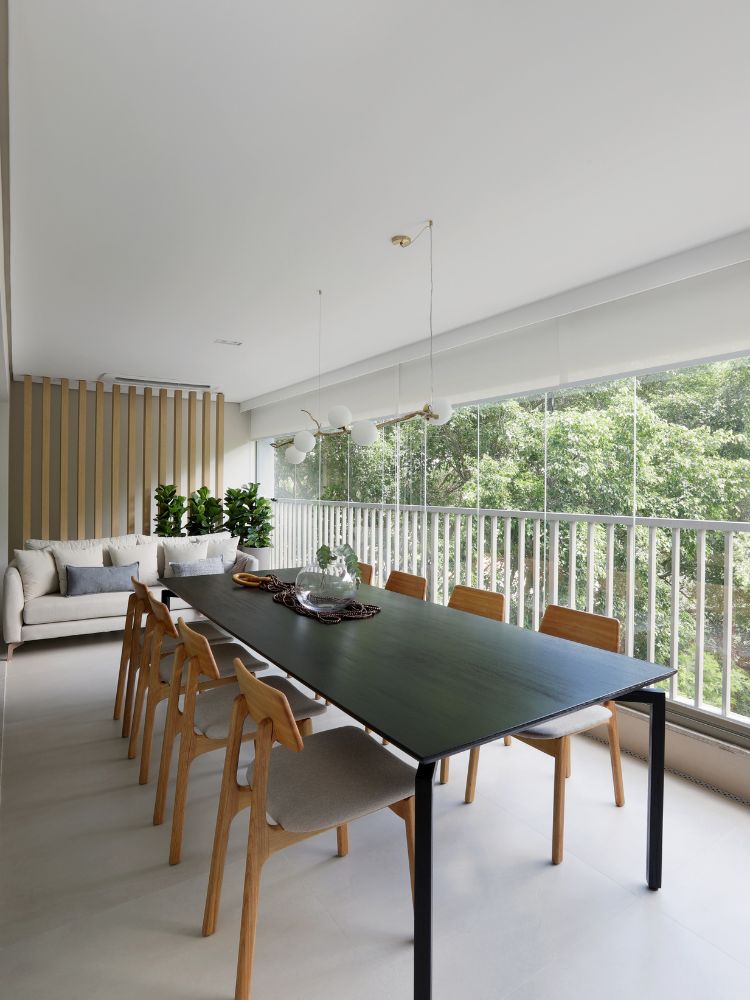 Apartamento-Decorado-158-M2-7 Terraço com painel ripado, sofá, grande mesa escura com cadeiras amadeiradas e vista para árvores