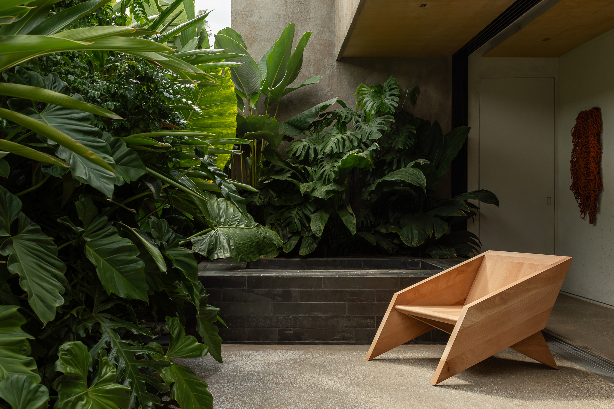 Jardim estreito integrado à área social da Casa Jasmim, projeto da MIDA Arquitetura, com vegetação densa e materiais naturais