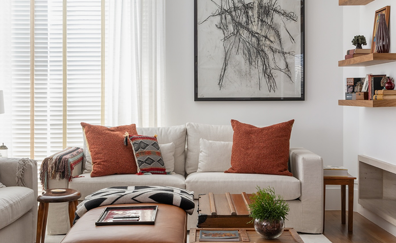Sala de estar com sofá claro, várias almofadas, objetos decorativos à vista e diferentes estímulos visuais no ambiente.