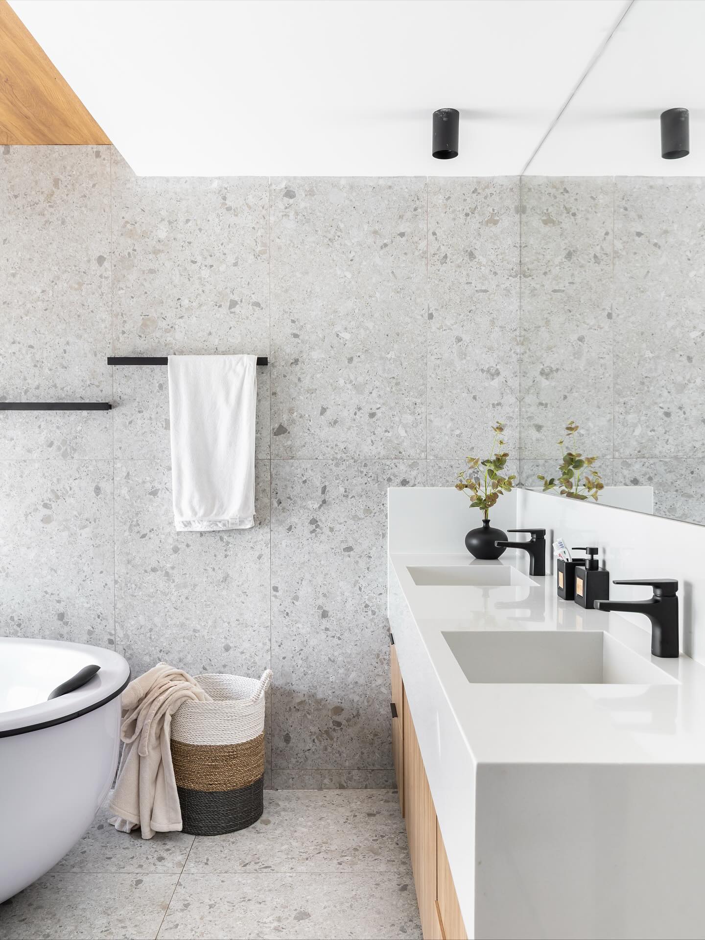 Banheiro de casal com revestimentos claros e madeira, criando sensação de conforto.