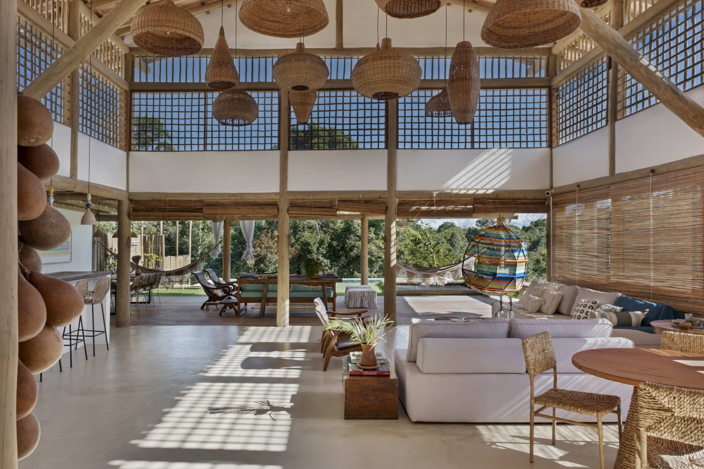 Sala de estar com pé-direito duplo, estrutura em madeira e vista integrada para a natureza em casa de praia