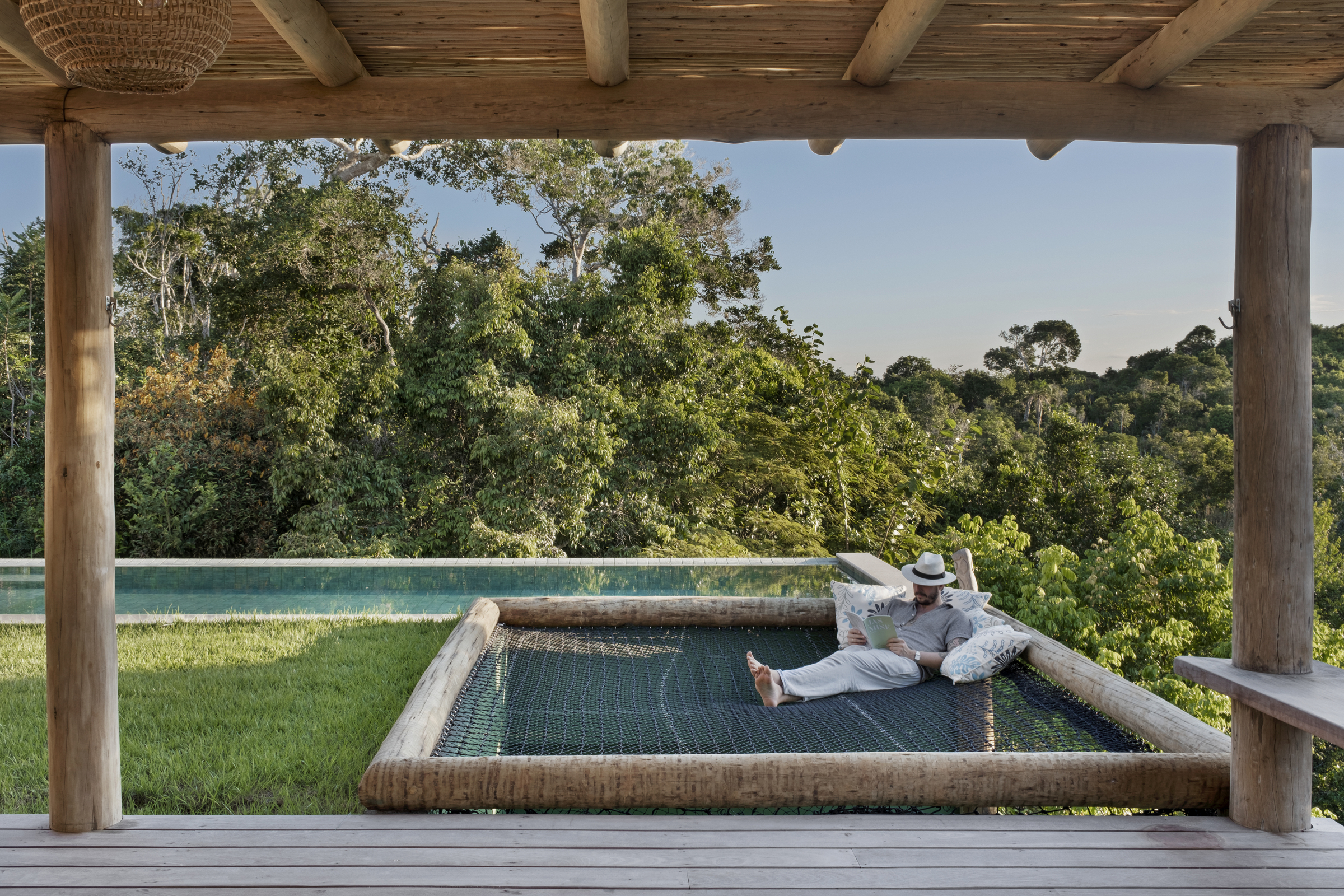 Área externa com deck de madeira, piscina integrada e vista para a mata em casa de praia em Trancoso