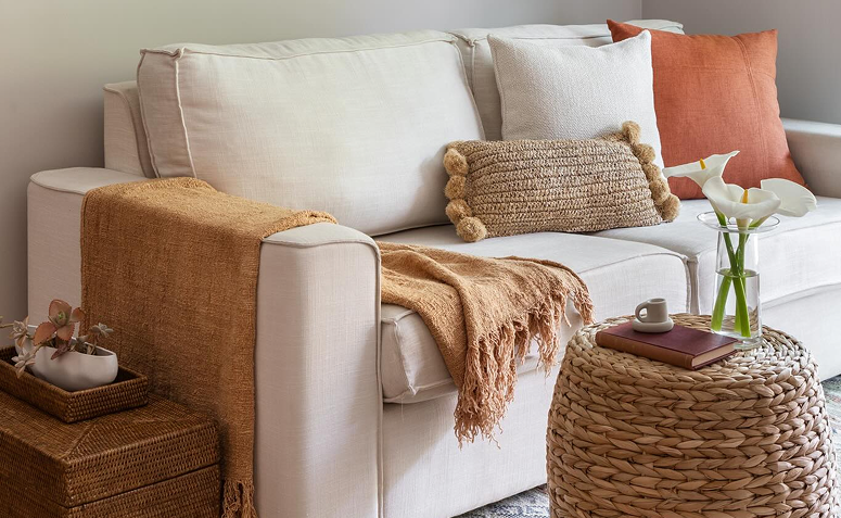 Sala de estar com tecidos e texturas naturais e almofadas claras.