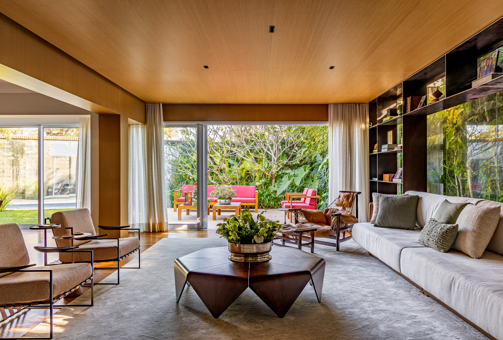 Sala de estar integrada ao jardim com painel de vidro e tons terrosos.