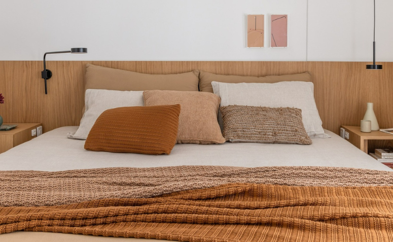 cama de casal arrumada, com lençol claro, sobreleito e almofadas em tons de laranja.