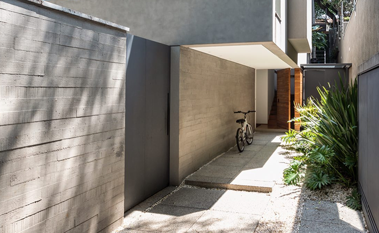 Corredor externo com piso de concreto e paredes em acabamento bruto, destacando os revestimentos e a arquitetura do espaço.