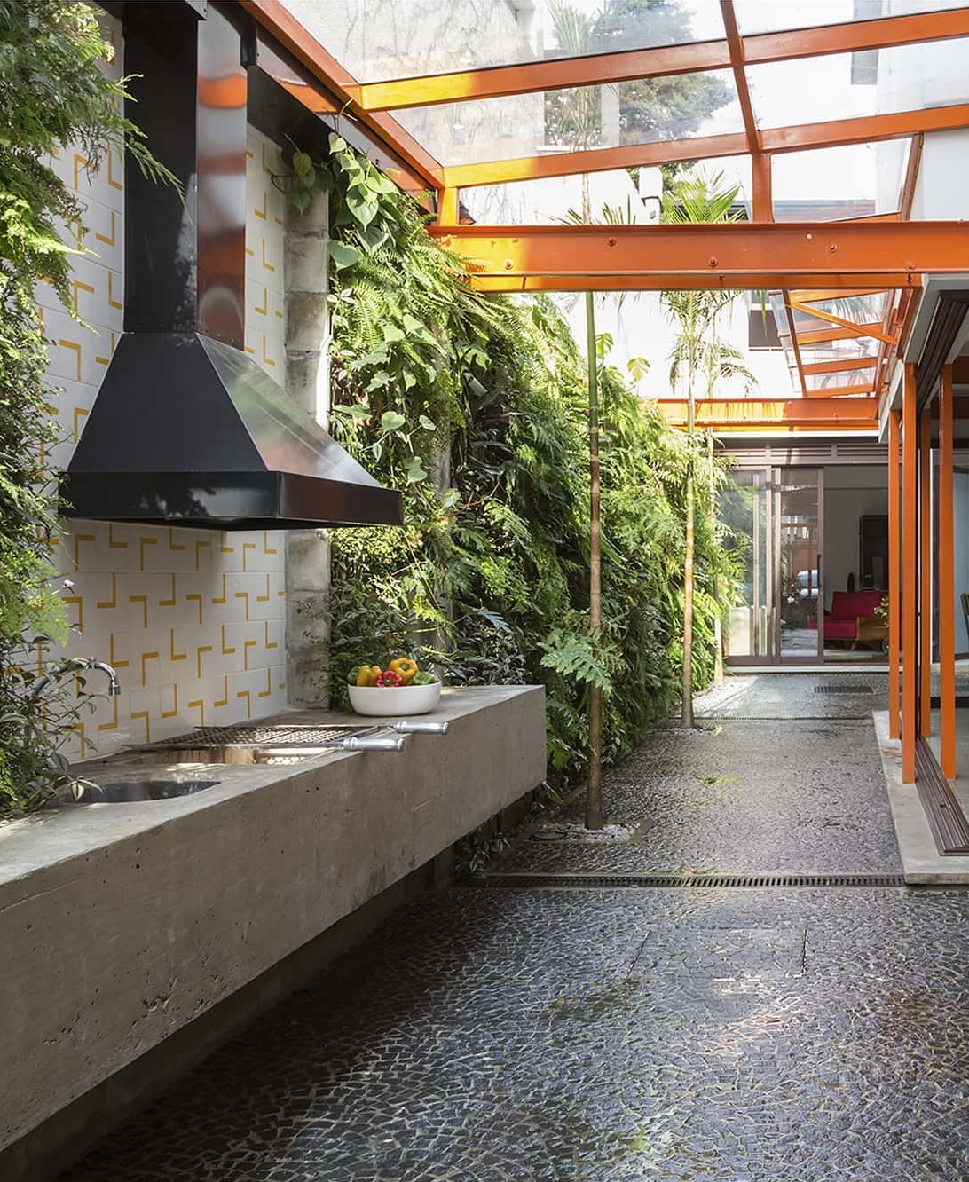 Corredor externo com paisagismo lateral e estrutura arquitetônica criando um percurso entre os volumes da casa.