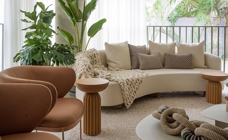 Sala com sofá e almofadas em tecidos naturais, manta de trama grossa e tapete neutro na decoração