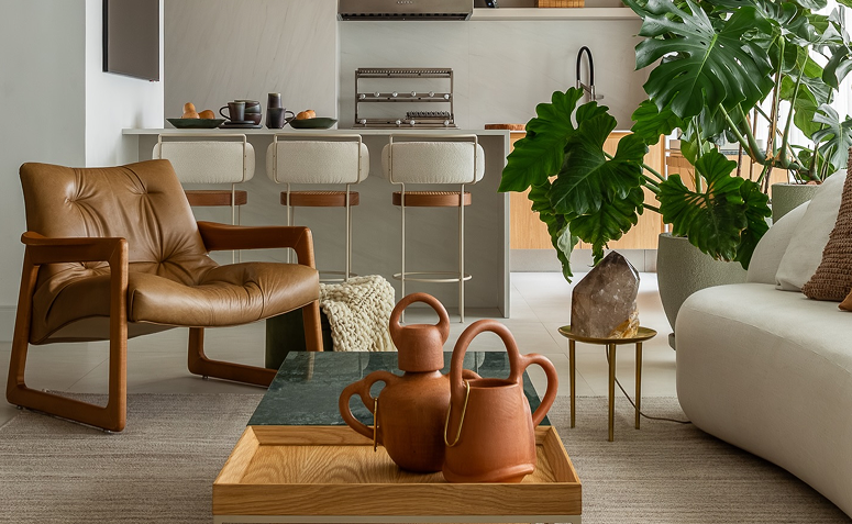 Sala com poltrona de couro, mesa de madeira e bancada com banquetas metálicas combinando materiais naturais e modernos