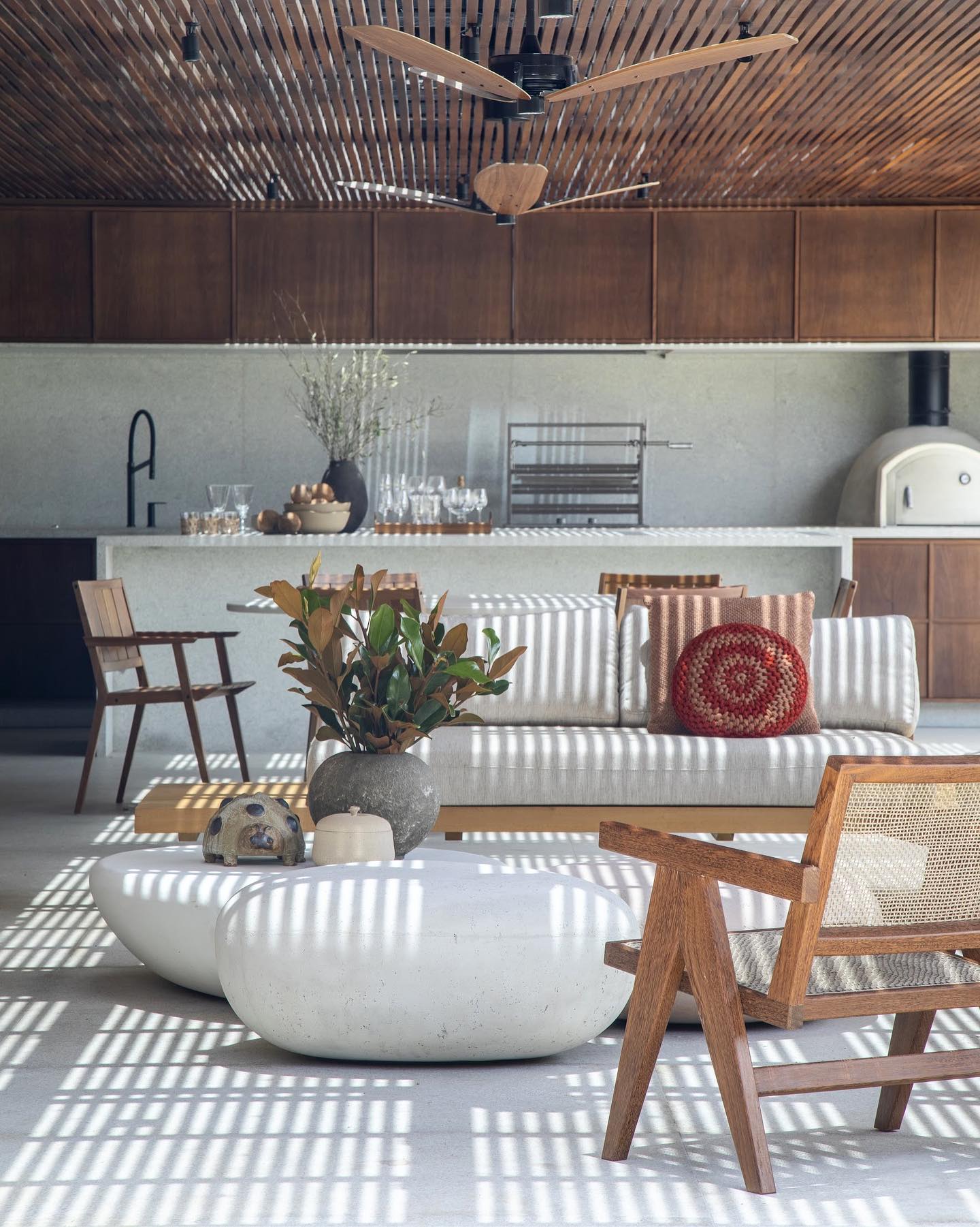 Varanda com teto ripado de madeira, móveis de madeira e mesa de centro de pedra em ambiente com texturas naturais