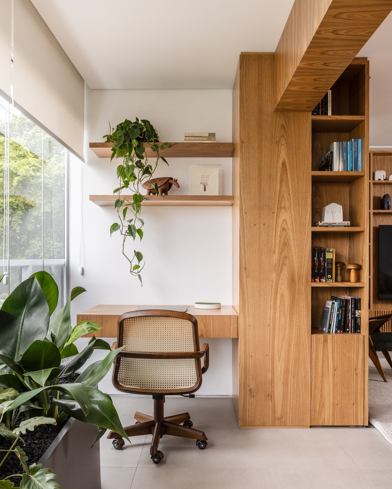 Espaço de trabalho com mesa de madeira, cadeira de palhinha, prateleiras de madeira e plantas na decoração