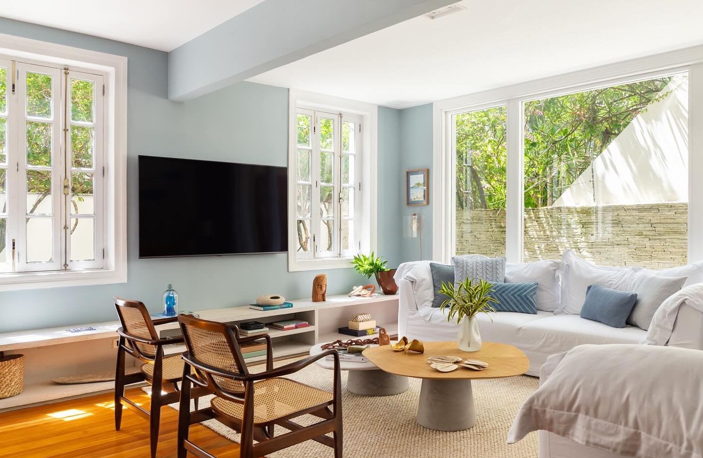 Sala de estar com poltronas de palhinha, mesa de centro de madeira, sofá branco e plantas na decoração