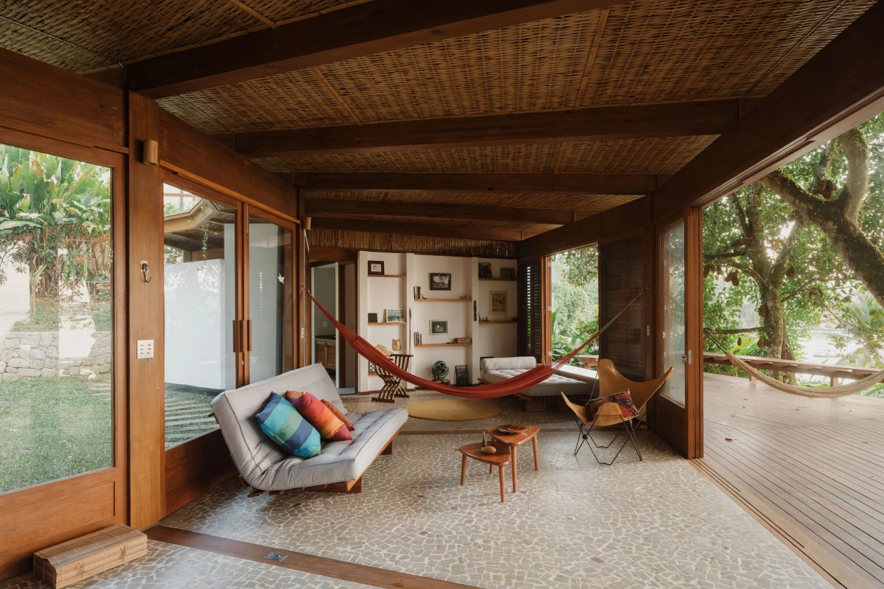 sala integrada com rede e abertura para o deck com vista para o pôr do sol em casa na mata em angra dos reis
