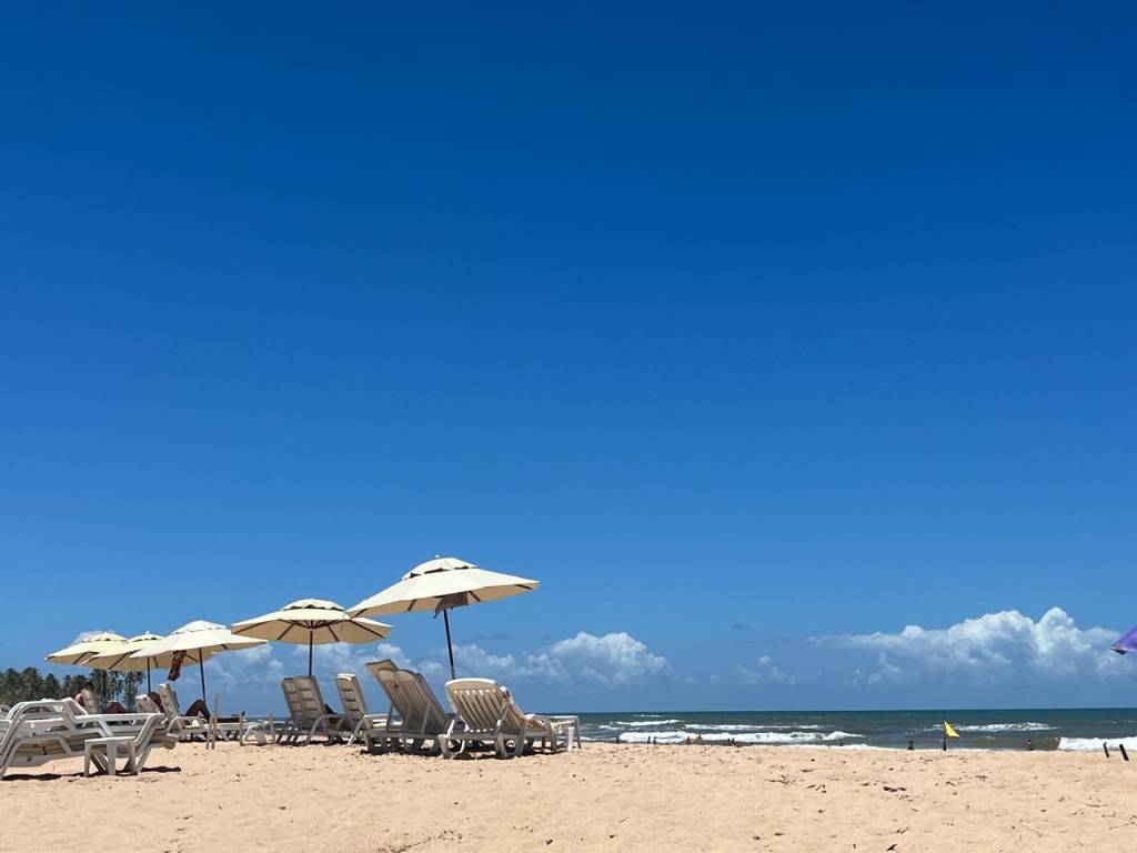 Espreguiçadeiras e guarda-soís na beira de uma praia de areia fina e água azul