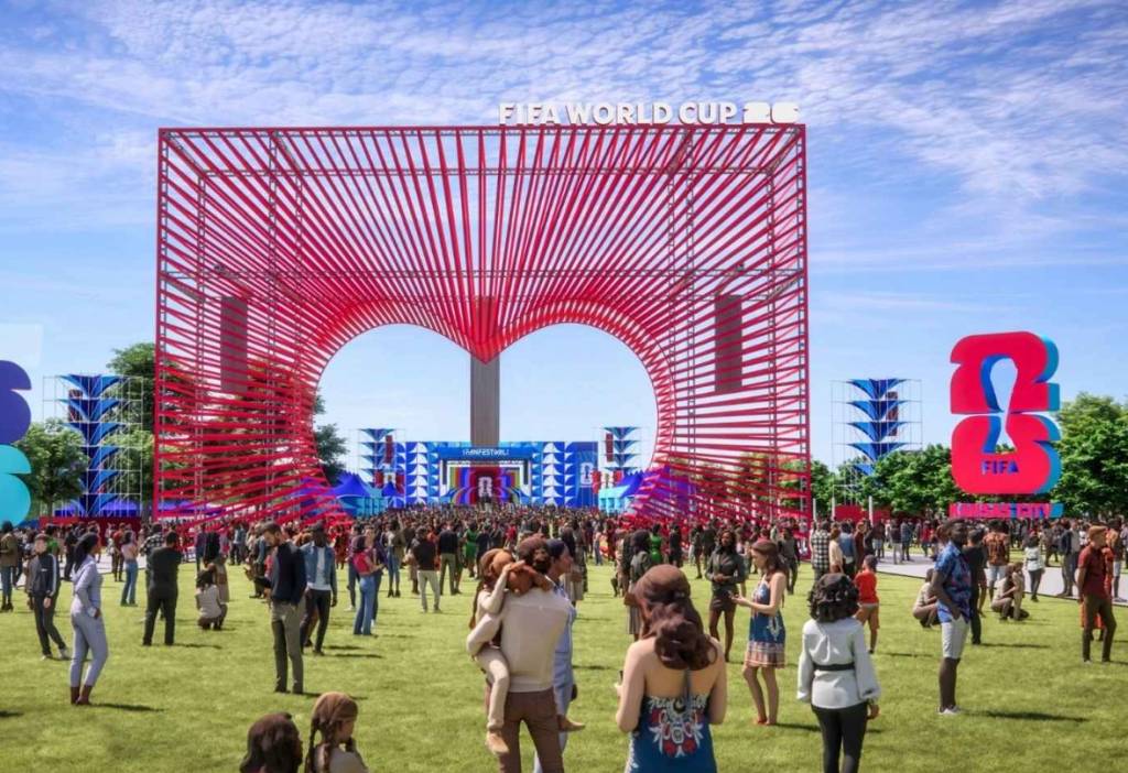 Multidão em um gramado verde, com uma estrutura vermelha gigante em forma de coração ao fundo, exibindo
