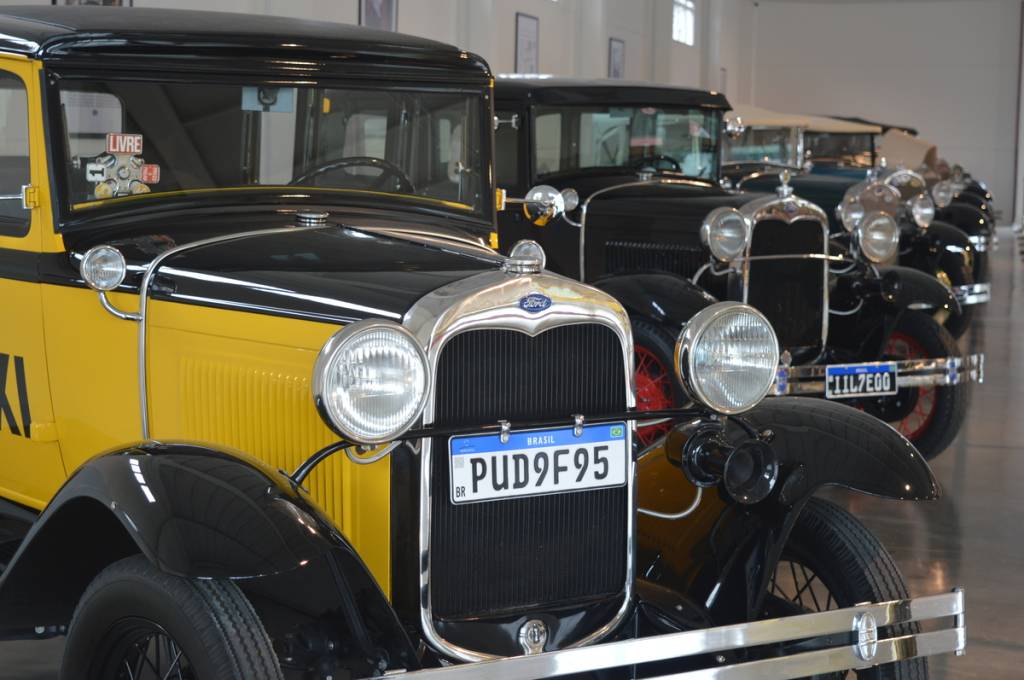Fileira de carros antigos pretos e amarelos, com detalhes cromados e faróis redondos, em exposição