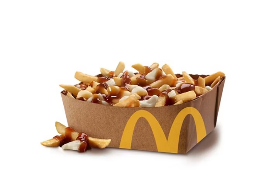 Porção de poutine do McDonald's em uma embalagem de papelão marrom com o logotipo amarelo da marca, cheia de batatas fritas douradas, pedaços de queijo coalho branco e molho gravy escuro, com algumas batatas e queijo caídos na base branca