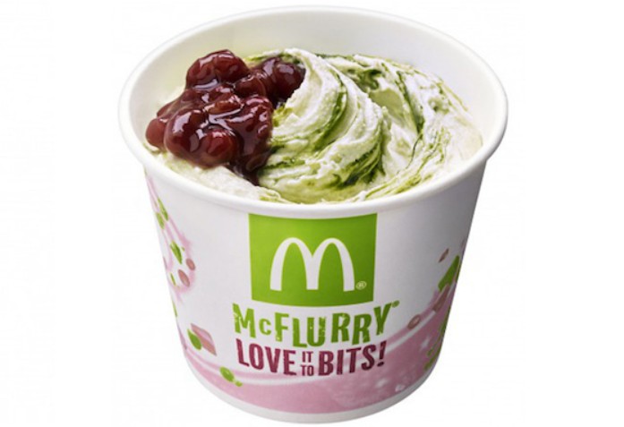 Copo de McFlurry com sorvete de baunilha e matcha, coberto com calda de feijão azuki, sobre fundo branco. O copo tem o logo do McDonald's e a frase