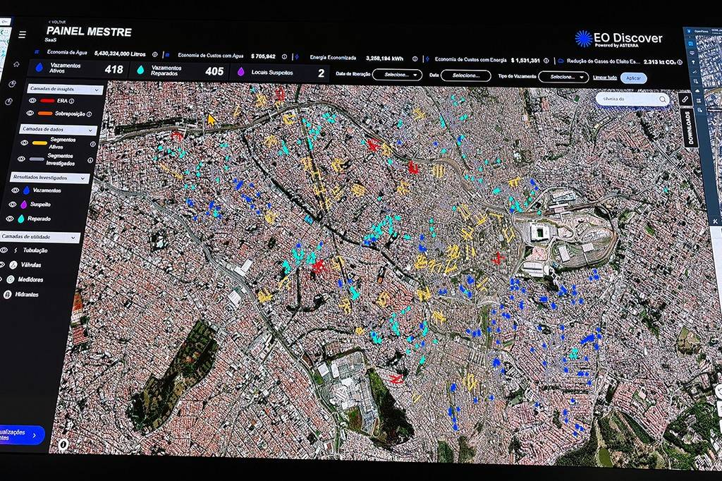 Tela de computador exibindo um mapa de satélite de uma cidade com áreas coloridas em vermelho, azul, amarelo e ciano, indicando vazamentos de água ativos e reparados, locais suspeitos e outras informações. No topo, um painel com dados como Vazamentos Ativos 418 e Vazamentos Reparados 405. À esquerda, um menu com Camadas de insights, Camadas de dados, Resultados investigados e Camadas de utilidade. No canto superior direito, o logo EO Discover Powered by ASTERRA
