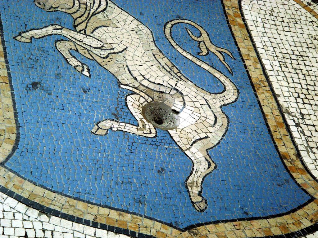 Mosaico de chão com um touro branco empinado sobre um fundo azul, contornado por uma borda bege e preta, em um piso de ladrilhos brancos