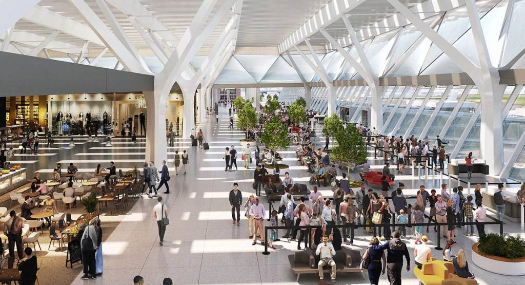 Interior de um aeroporto moderno e espaçoso, com teto alto de vidro e estrutura branca. Muitas pessoas circulam e aguardam em áreas de assento e restaurantes, algumas com malas. Há lojas e árvores decorativas, criando um ambiente iluminado e movimentado