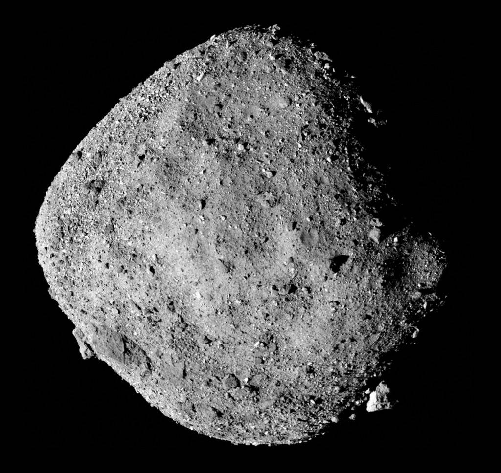 Asteroide Bennu, rochoso e irregular, em tons de cinza, com superfície coberta por pedras e crateras de diversos tamanhos, flutuando no espaço escuro