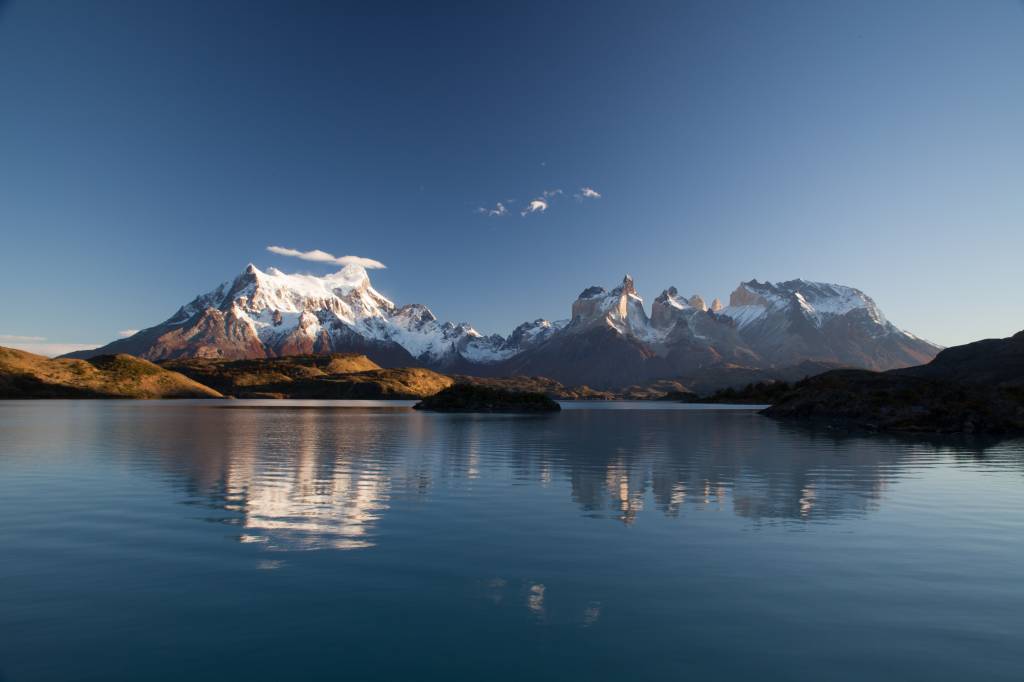 A imagem mostra uma formação montanhosa nevada atrás de um lago