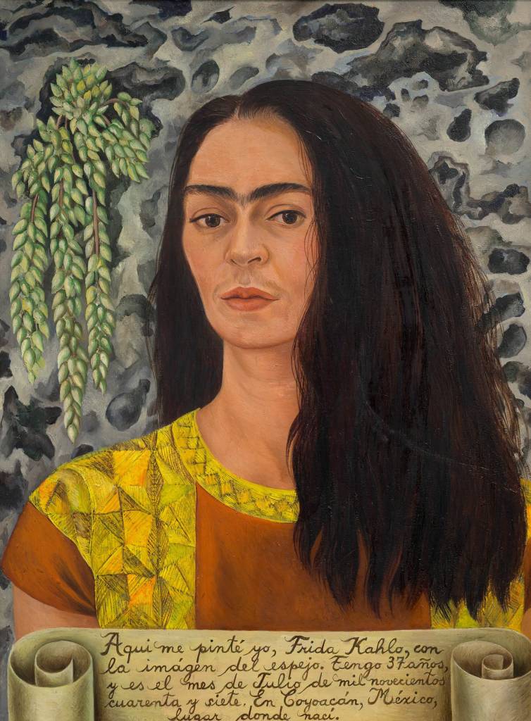 Autorretrato de Frida Kahlo, com cabelos longos e escuros, sobrancelhas unidas, vestindo blusa marrom e amarela. Ao fundo, uma planta pendente e parede cinza. Abaixo, um pergaminho com texto em espanhol