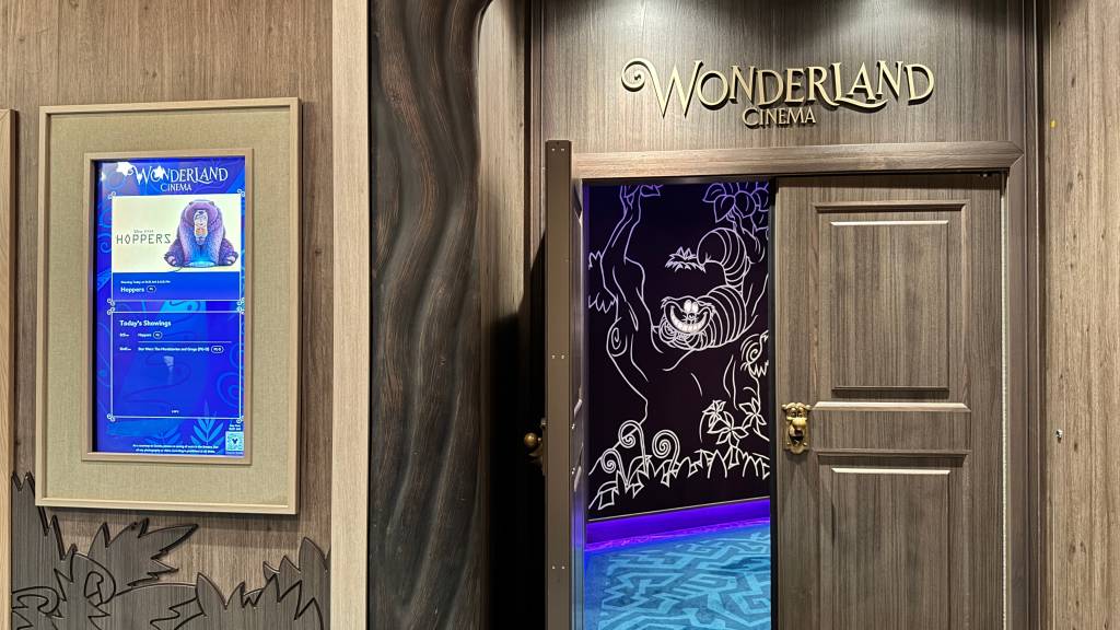 Entrada do cinema Wonderland com uma tela digital exibindo o filme Hoppers e uma porta de madeira com o Gato de Cheshire desenhado em luz neon branca