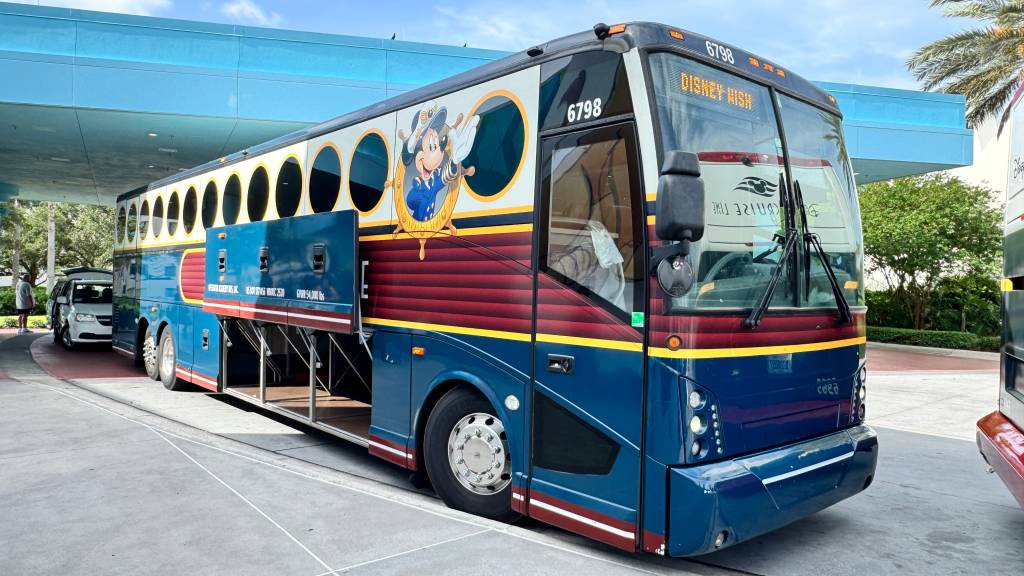 Ônibus azul e vermelho da Disney Cruise Line com o Mickey Mouse marinheiro na lateral, parado em um terminal com compartimentos de bagagem abertos