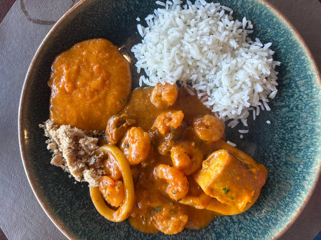 Prato com moqueca de camarão e lula em molho laranja, acompanhada de arroz branco soltinho, pirão e farofa, servido em um prato azul-esverdeado
