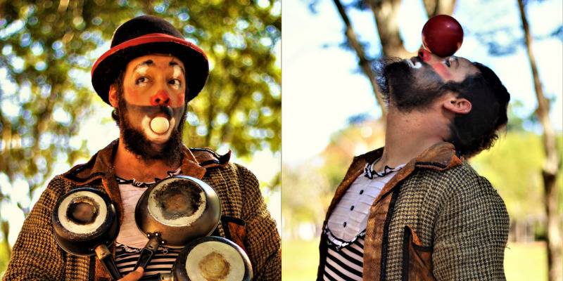 Um homem com barba e maquiagem de palhaço, usando chapéu e casaco xadrez, segura panelas e equilibra uma bola vermelha no nariz