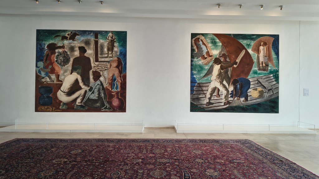 Duas pinturas em estilo muralista, com figuras humanas em tons terrosos e azuis, expostas em uma parede branca de galeria, com um tapete persa vermelho no chão