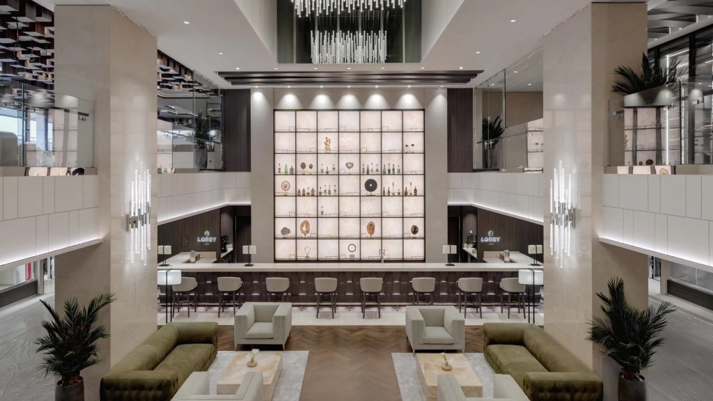 Lobby de hotel moderno e luxuoso com balcão de bar iluminado, estantes com garrafas e objetos decorativos, sofás e poltronas em tons neutros, e plantas ornamentais